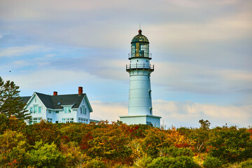 Fototapeta na wymiar Large lighthouse by home in colorful fall forest with overcast sky