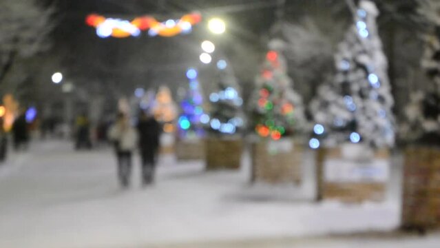 People walk along street decorated Christmas trees with luminous decorations, illuminations and hanging street decorations during heavy snowfall on winter night. Christmas New Year. Blurred background