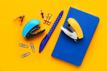 Bright staplers and stationery on color background