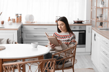 Young woman reading book at dining table in kitchen