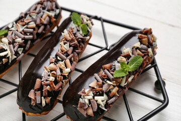 Grid with delicious chocolate eclairs on white wooden table, closeup