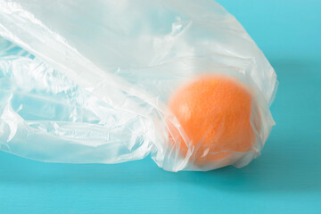 Orange in a plastic bag on a turquoise background