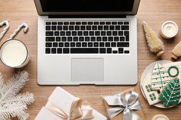 Laptop with Christmas decor, glass of milk, cookies and gifts on wooden background