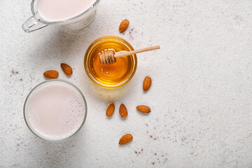 Glass of healthy almond milk, bowl with honey and nuts on light background