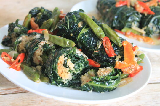 Indonesian food called buntil daun pepaya made of Papaya leaf, chilli, tomato,coconut,and ikan teri in white plate on wooden table