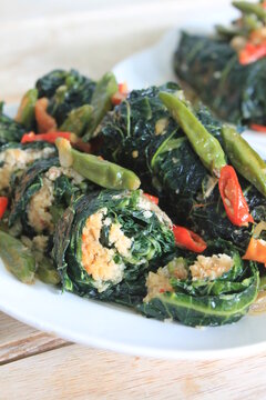 Indonesian food called buntil daun pepaya made of Papaya leaf, chilli, tomato,coconut,and ikan teri in white plate on wooden table