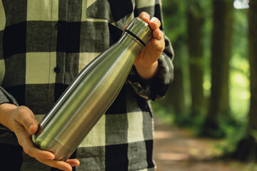 Close-up of Unrecognizable female hand holding Water bottle. Reusable steel thermo water bottle in...