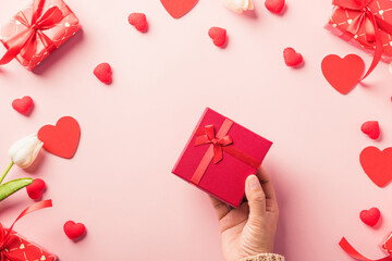 Valentine's day and birthday. Woman hands holding gift or present box decorated and red heart surprise on pink background, Female's hand hold gift box package in craft paper Top view flat lay