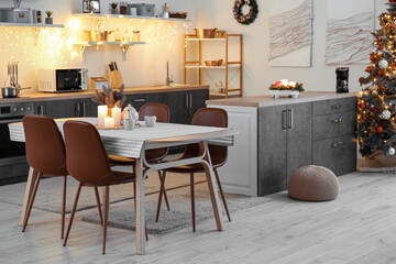 Interior of kitchen with glowing Christmas tree, counters and dining table