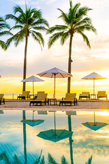 Umbrella and chair around swimming pool in hotel resort with sunrise in morning