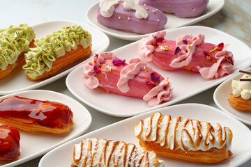 Set of colored eclairs with whipped cream on white plates