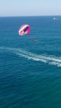 Vertical video of Aerial shot of a parasailing boat going over turquoise water