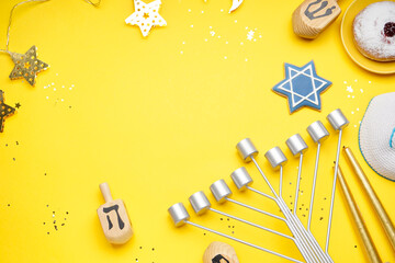 Frame made of menorah, treats, dreidels and stars for Hannukah celebration on yellow background