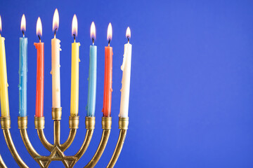 Menorah with burning candles for Hannukah celebration on blue background, closeup