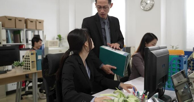 asian woman worker rejecting doing extra paperwork for manager. she points at her watch and complains she is already working to a tight deadline