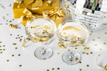 Glasses of champagne, Christmas balls and gifts on white background, closeup