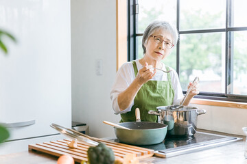 家のキッチンで料理を作るアジア人の高齢者女性（認知症・悩む）
