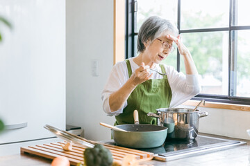 家のキッチンで料理を作るアジア人の高齢者女性（認知症・悩む）
