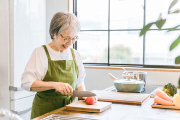 家のキッチンで料理を作るアジア人の高齢者女性
 - obrazy, fototapety, plakaty
