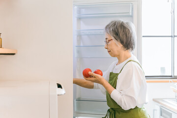 家のキッチンで料理を作るため冷蔵庫から野菜を出すアジア人の高齢者女性
