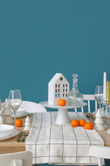 Christmas table setting with candle holders and mandarins near blue wall