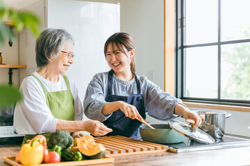 家のキッチンで一緒に料理・家事・自炊をする笑顔のアジア人高齢者女性と若い女性（家政婦・家事代行）
