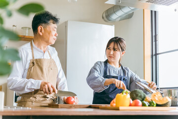 家のキッチンで怒るアジア人高齢者男性と若い女性（家政婦・家事代行）
