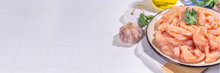 Cooking diet white poultry meat background. Fresh sliced chicken strips raw for cooking, with spices, herbs, on a white tile background top view copy space