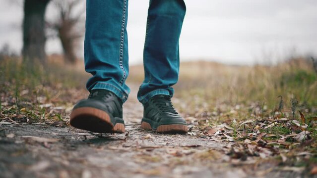 Man walks on wooded area on hike for walk in autumn outdoors nature landscape. Close up of man's legs. Active rest and sports walking. Healthy lifestyle at leisure activity. Ground with fall foliage.
