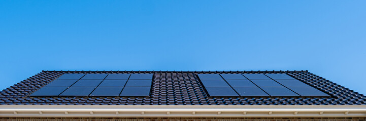 Newly build houses with black solar panels attached to the roof against a sunny blue sky in the...