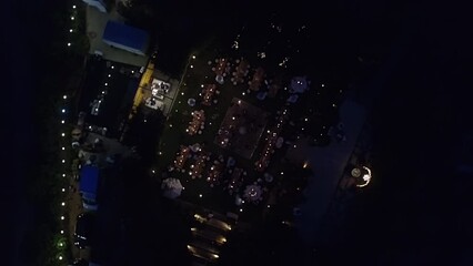 Drone footage of a beautiful garden decorated for wedding reception. Charming, warm lighting around party and dinner setting outdoors as seen at night. High quality 4k footage