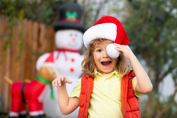 Obraz premium Happy New Year and merry Christmas. Funny kid in santa hat play in front of a house.