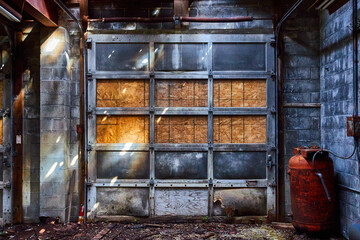 Fototapeta na wymiar Detail of abandoned interior mechanic shop with gray garage door and red canisters