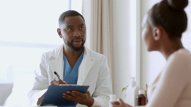 Black woman sitting at clinic and telling symptoms to therapist, african american doctor filling medical history