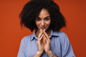 Tricky african american woman clasping hands isolated over red wall