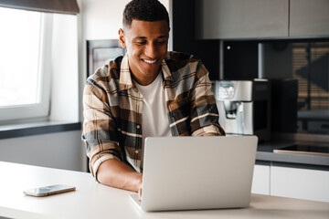 Cheerful african man using laptop while sitting at home