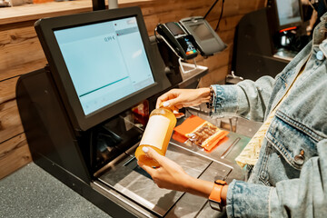 A girl customer scanns and pays for bottle of juice from a supermarket in an automated self-service...