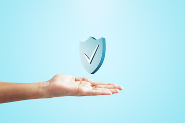 Close up of female hand holding creative antivirus shield icon on light blue background. Secure...