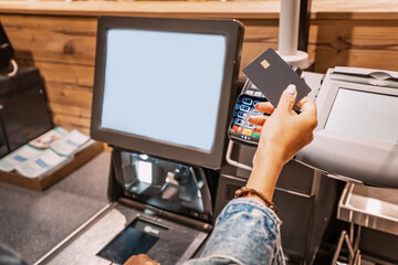 The girl buyer applies a credit card to the pos terminal to pay for purchases at the self-service checkout - obrazy, fototapety, plakaty