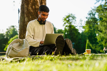 Young smiling african man working on laptop while sitting outdoors in park