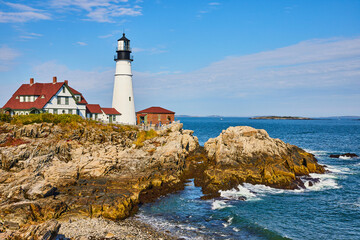 Beautiful white lighthouse in Maine on rocky coastline with ocean waves