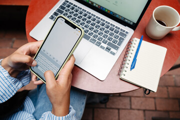 Close up of female hands using smartphone and laptop in cafe