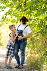 Fototapeta premium Pregnant woman walking countryside with her son. Child hugging his pregnant mother.