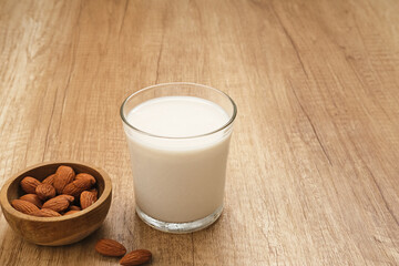 Almond milk in glass with almonds on wooden table. Space for text
