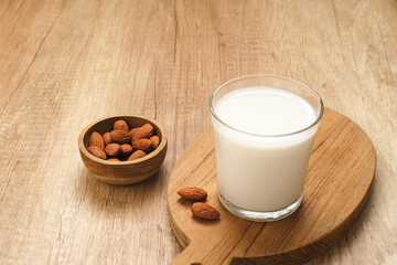 Almond milk in glass with almonds on wooden table. Space for text
