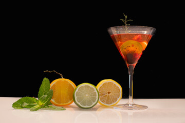 Verre à cocktail de couleur rouge avec des fruits sur fond noir.	
