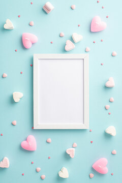 Valentine's Day concept. Top view vertical photo of photo frame heart shaped marshmallow candles and sprinkles on isolated pastel blue background with copyspace