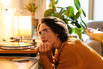 Young woman in eyeglasses listening music while sitting on floor