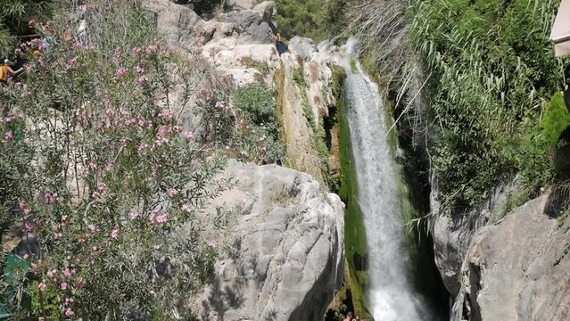 Fonts de L'Algar biggest cataract waterfall. Impressive water torrent plunge in rock cliff.Vegetation around. Tourist enjoying scenery. Ecotourism. Resources explotation.