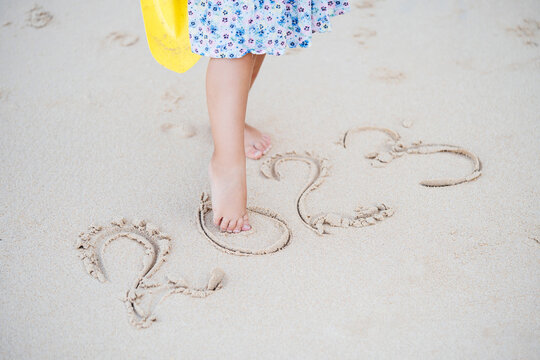 The concept of the new 2023. A child barefoot on a tropical sandy beach writes numbers.